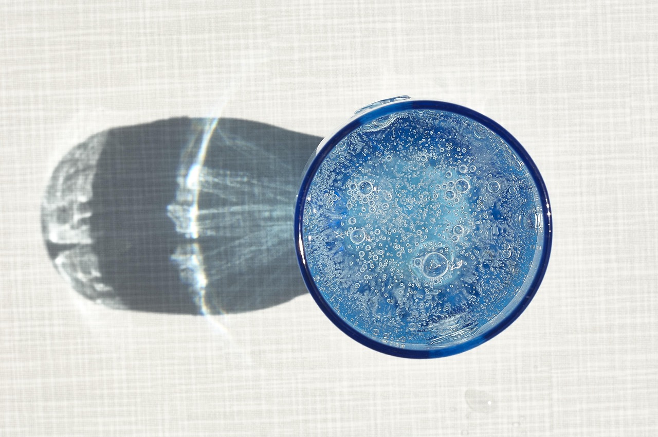 Acqua limpida in un bicchiere con riflessi brillanti su sfondo bianco.